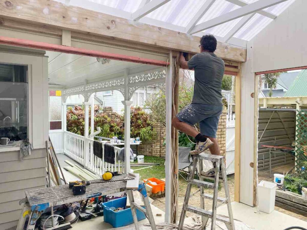 Frosted polycarbonate roofing being installed on new outdoor room with electrical wiring visible.