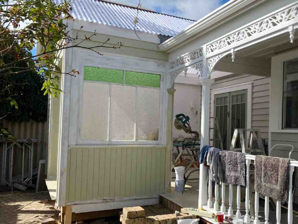 Repurposed coloured glass window providing privacy and light in a renovated outdoor room.